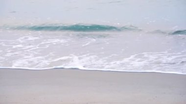 Köpüklü dalgaların kumsala doğru ağır çekimde yuvarlanması, altın plajın derin mavi okyanus suyu ve köpüklü dalgalarla buluşması. Turkuaz deniz dalgaları kumlu sahil şeridinde kırılıyor. 