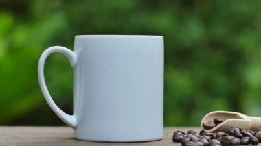 Eski ahşap bir masada kahve fincanı ve kahve çekirdekleri, beyaz bir seramik bardak..