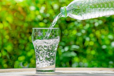 Plastik şişeden bardağa su dök. Bahçedeki bitkilerin arka planı. yumuşak odak.