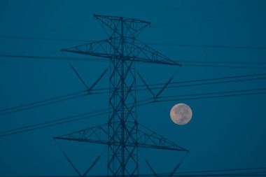 Yüksek voltaj direkleri ve dolunay arkaplanlı kablolar. yumuşak odak.