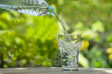 Plastik şişeden bardağa su dök. Bahçedeki bitkilerin arka planı. yumuşak odak.