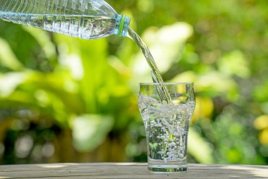 Plastik şişeden bardağa su dök. Bahçedeki bitkilerin arka planı. yumuşak odak.