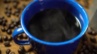 Eski ahşap zeminde kahve çekirdeği ve dumanlı bir bardak mineli kahve. Esrarlı kahve seti. yumuşak odak.