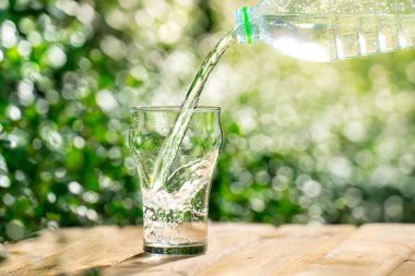 Plastik şişeden bardağa su dök. Bahçedeki bitkilerin arka planı. yumuşak odak.