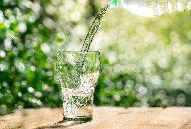 Plastik şişeden bardağa su dök. Bahçedeki bitkilerin arka planı. yumuşak odak.