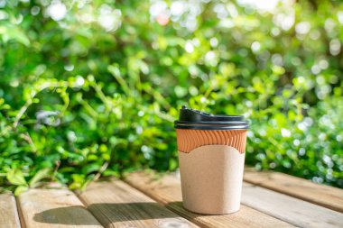 Kağıt kahve fincanı ahşap zeminde, yeşil ağaç bokeh arka plan sabah. Yumuşak odaklanma. Sığ odak etkisi.