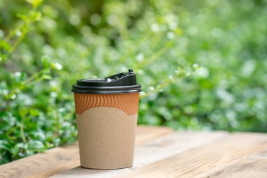 Tahta zeminde kağıt kahve fincanı, yeşil ağaç bokeh arka plan. Yumuşak odaklanma. Sığ odak etkisi.