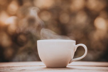 Ahşap zeminde beyaz seramik kahve fincanının eski tarz fotoğrafı, yeşil ağaç bokeh arka plan. Yumuşak odaklanma. Sığ odak etkisi.