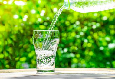 Plastik şişeden bardağa su dök. Bahçedeki bitkilerin arka planı. yumuşak odak.