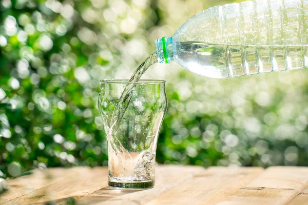 Pour water from a plastic bottle into a glass. The background of the plants in the garden. soft focus.