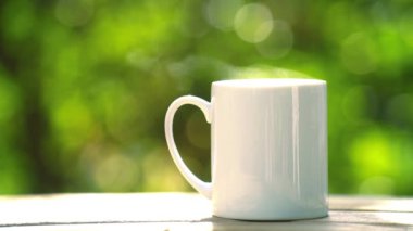 white ceramic coffee mug On the wooden floor, green tree bokeh background