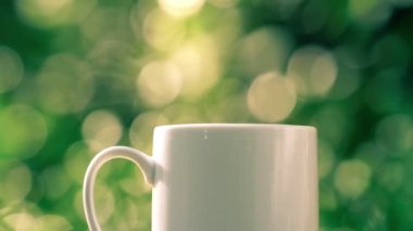 Ahşap zeminde beyaz seramik kahve kupası, yeşil ağaç bokeh arka plan. Yumuşak odaklanma. Sığ odak etkisi.