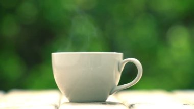 Ahşap zeminde beyaz seramik kahve kupası, yeşil ağaç bokeh arka plan. Yumuşak odaklanma. Sığ odak etkisi.