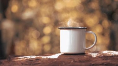 Hot coffee mug with smoke on wooden table against green trees