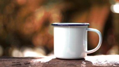 Hot coffee mug with smoke on wooden table against green trees