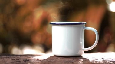 Hot coffee mug with smoke on wooden table against green trees