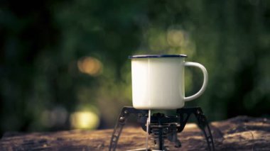 Hot coffee mug with smoke on wooden table against green trees