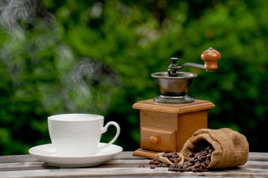 Öğütücüyle kahve fincanı, eski ahşap zeminde kahve çekirdekleri, doğal bir arka planda kahve çekirdekleri.. 