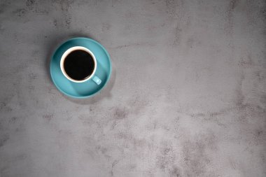 Eski gri çimento zeminde mavi seramik bir fincanda sade kahve.