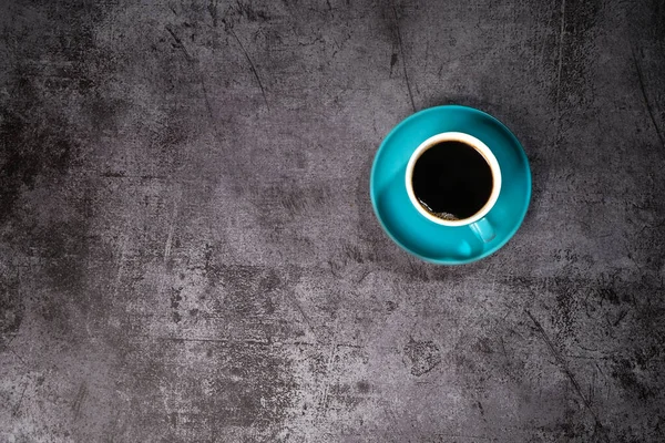 Eski gri çimento zeminde mavi seramik bir fincanda sade kahve.