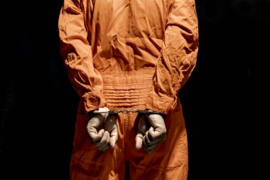 Handcuffs on Accused Criminal in Orange Jail Jumpsuit. Law Offender Sentenced to Serve Jail Time, in black background