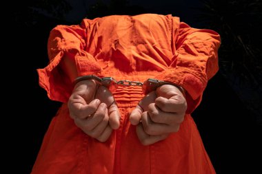 Handcuffs on Accused Criminal in Orange Jail Jumpsuit. Law Offender Sentenced to Serve Jail Time, in black background