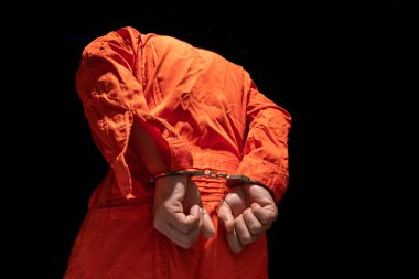 Handcuffs on Accused Criminal in Orange Jail Jumpsuit. Law Offender Sentenced to Serve Jail Time, in black background