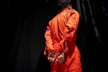 Handcuffs on Accused Criminal in Orange Jail Jumpsuit. Law Offender Sentenced to Serve Jail Time, in black background