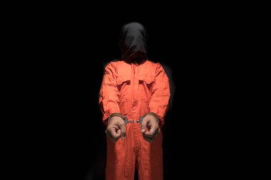 Handcuffs on Accused Criminal in Orange Jail Jumpsuit. Law Offender Sentenced to Serve Jail Time, in black background