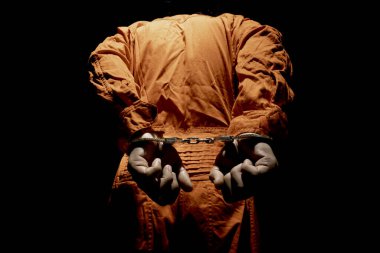 Handcuffs on Accused Criminal in Orange Jail Jumpsuit. Law Offender Sentenced to Serve Jail Time, in black backgroun