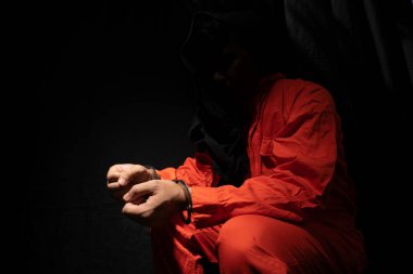 Handcuffs on Accused Criminal in Orange Jail Jumpsuit. Law Offender Sentenced to Serve Jail Time, in black backgroun