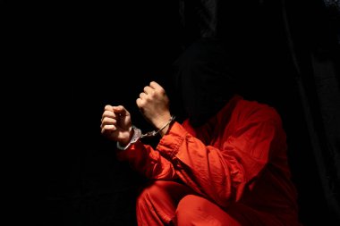 Handcuffs on Accused Criminal in Orange Jail Jumpsuit. Law Offender Sentenced to Serve Jail Time, in black backgroun