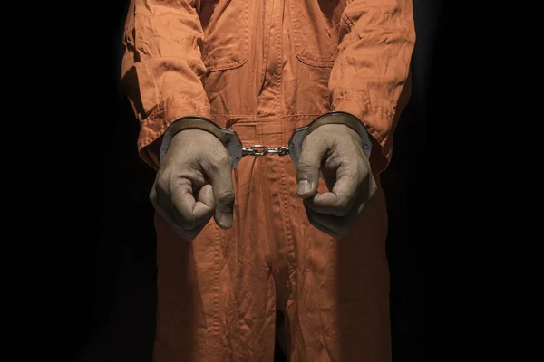 Handcuffs on Accused Criminal in Orange Jail Jumpsuit. Law Offender Sentenced to Serve Jail Time, in black background