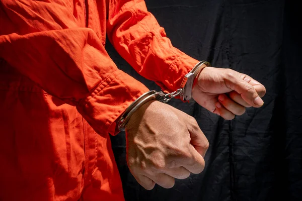 Handcuffs on Accused Criminal in Orange Jail Jumpsuit. Law Offender Sentenced to Serve Jail Time, in black background