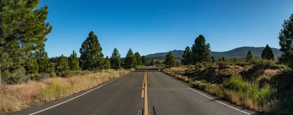 Two lane road runs straight through a mountain meadow in the woods of northern California.
