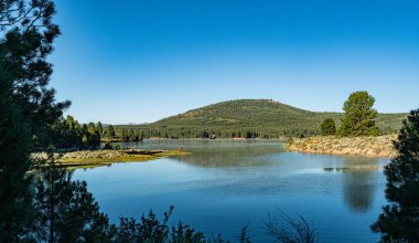 Hillside reflected in a Calm California lake water blue.