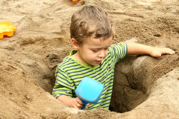 Kleine jongen in een gegraven uit zand gat — Stockfoto