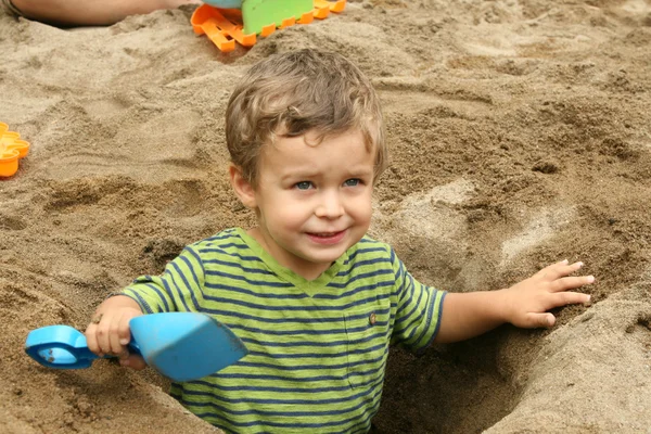 Kleine jongen in een gegraven uit zand gat Stockfoto