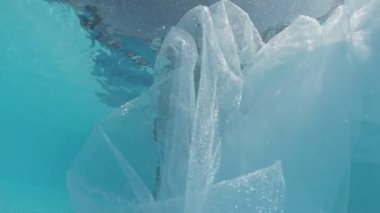 Siyah mayo giymiş genç bir kadın ve açık havuzun dibinde mavi fayanslarla süslenmiş beyaz bir pelerin duruyor..