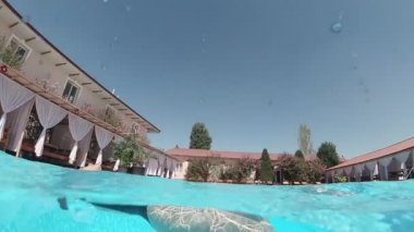 Siyah mayo giymiş genç bir kadın ve açık havada yüzme havuzunda mavi fayanslarla süslenmiş beyaz bir pelerin yüzüyor..