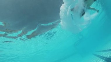 Siyah mayo giymiş genç bir kadın ve açık havada yüzme havuzunda mavi fayanslarla süslenmiş beyaz bir pelerin yüzüyor..