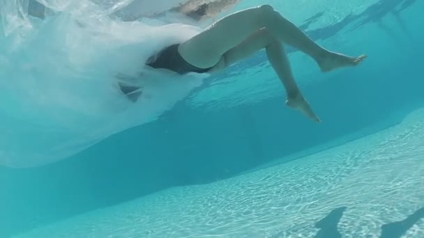 身穿黑色泳衣和白色长袍的年轻女子在装饰着蓝色瓷砖的室外游泳池游泳 — 图库视频影像