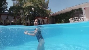 Siyah mayo giymiş genç bir kadın ve açık havada yüzme havuzunda mavi fayanslarla süslenmiş beyaz bir pelerin yüzüyor..