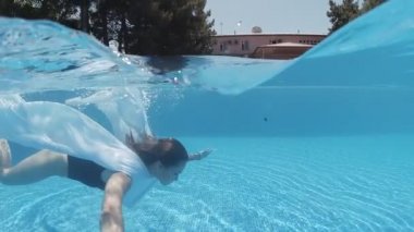 Siyah mayo giymiş genç bir kadın ve açık havada yüzme havuzunda mavi fayanslarla süslenmiş beyaz bir pelerin yüzüyor..