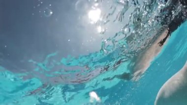 Siyah mayo giymiş genç bir kadın ve açık havada yüzme havuzunda mavi fayanslarla süslenmiş beyaz bir pelerin yüzüyor..