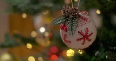Kırmızı kar taneleriyle süslenmiş beyaz, yumuşak noel balosu. Çam kozalaklarıyla süslenmiş Noel ağacı. Arkasında yanıp sönen bir çelenk