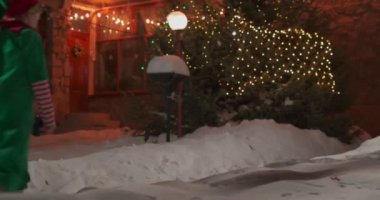 Karlı bir Noel arifesinde sokakta iki çocuk. Arkadaki dekore edilmiş ev, ağır çekimde.