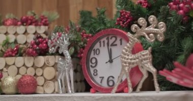 Pink shiny clocks between silver christmas deer toys in front of the christmas tree, slow motion