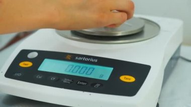 Closeup of polymer thread sample is weighted on electronic scales, slow motion