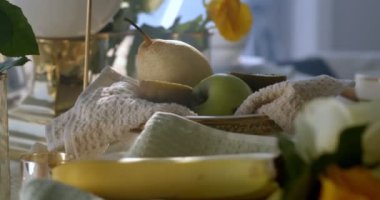Kitchen still life which consists of pear, green apple and two halves of a kiwi lying on the kitchen towel in a white and gold fruit vase. There is a banana on the front. Filmed under soft daylight.